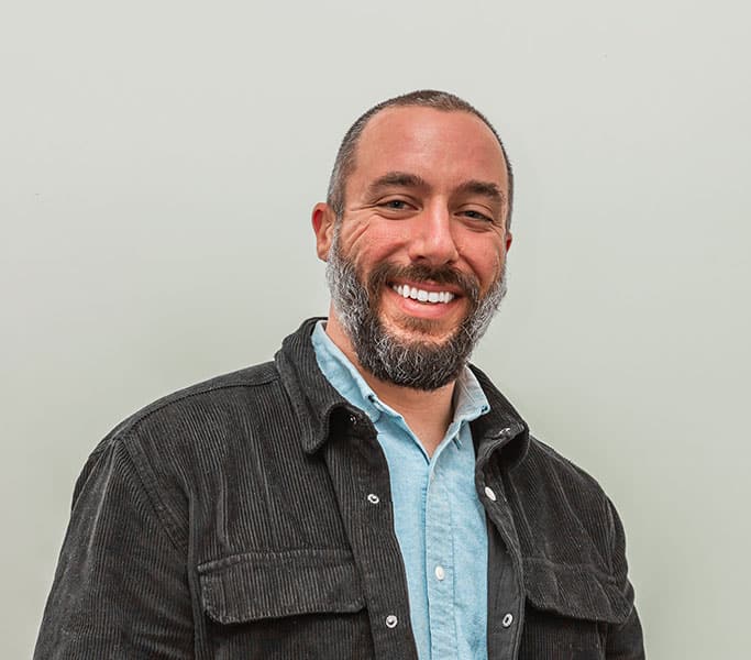 Smiling man with a beard against a light background.